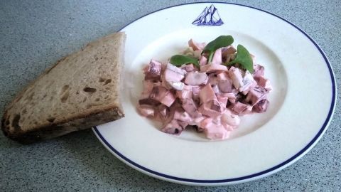 Ein Teller mit Wintersalat aus Roter Bete und frisch gehacktem Gemüse liegt neben einer Scheibe Brot auf einem Tisch.