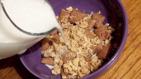 In einer lila Schüssel wird Milch energiesparend über knusprige Cerealien gegossen, um ein Frühstück zuzubereiten.