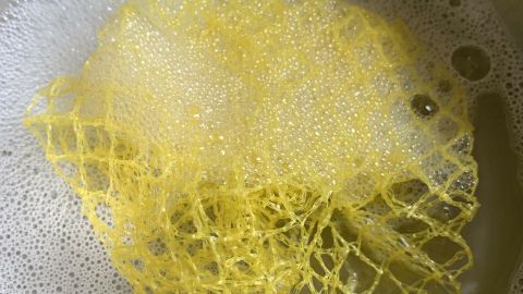 Ein gelbes Netz von Obst oder Gemüse schwimmt in einem Topf mit Seifenwasser, um als Spüllappen wiederverwendet zu werden.