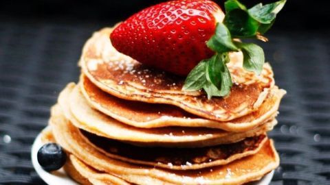 Stapels von amerikanischen Pancakes sind auf einem weißen Teller angerichtet, garniert mit einer Erdbeere und Minze.