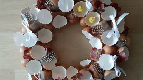 Ein dekorativer Osterkranz aus Eierschalen und bunten Elementen liegt auf einer hellen Oberfläche.