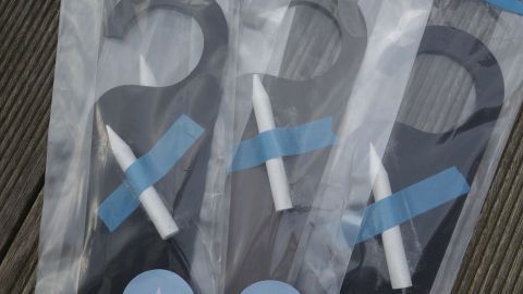 Schlichte Türanhänger aus Karton liegen in durchsichtigen Tüten auf einem Holzuntergrund und sind als Give-away verpackt.