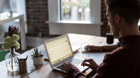Ein Mann arbeitet am Laptop in einem hellen Raum mit Pflanzen und einer Tasse, während er Ideen für das Home Office notiert.