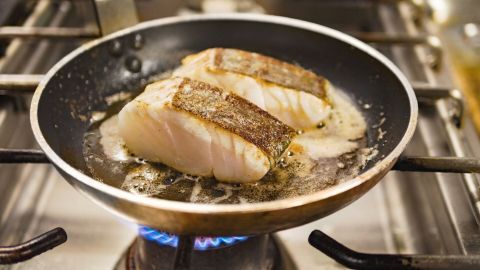 Im Bratpfanne braten zwei Fischfilets in erhitztem Öl, während sie auf einem Herd für die Zubereitung vorbereitet werden.