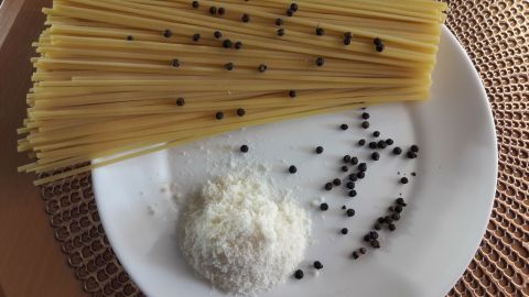 Spaghetti liegen auf einem Teller, während Salz und Pfeffer daneben gestreut sind, bereit für ein vegetarisches Gericht.