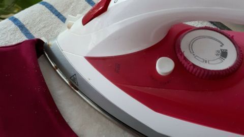 Ein rotes Bügeleisen liegt auf einem Tisch, während es einen dunkelroten Pulli mit Stehkragen bearbeitet, um ihn zu befestigen.