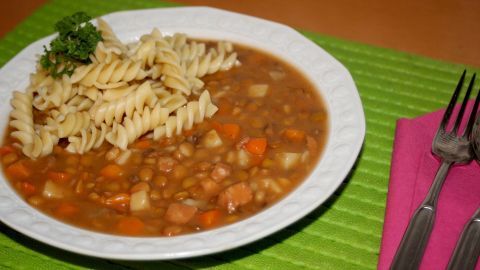 Nudeln liegen dekorativ neben einer schmackhaften Linsensuppe auf einem grünen Tischset, umgeben von Besteck.