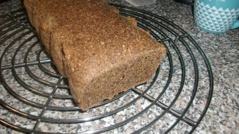 Ein vollwertiges Eiweißbrot liegt auf einem kühlenden Gitter, umgeben von einer grauen Arbeitsplatte und Tassen.