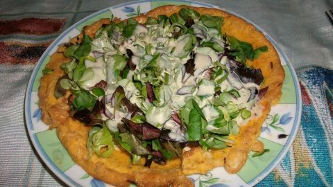 Ein Eieromelette ist auf einem Teller angerichtet und mit frisch geschnittenem Salat-Topping bedeckt, auf einem gemusterten Tisch.