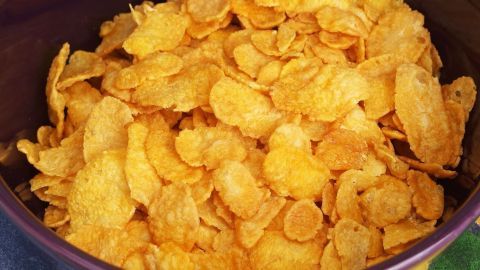 Statt einem alten Brötchen kann man in Milch eingeweichte Cornflakes zum Binden von Frikadellen verwenden. Goldene Cornflakes füllen eine Schüssel und werden für das Binden von Frikadellen vorbereitet, im Küchenumfeld sichtbar.