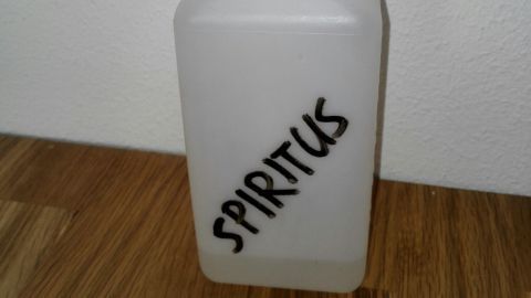 Eine Sprühflasche mit der Aufschrift "SPIRITUS" steht auf einem Holztisch und ist bereit, Desinfektionsmittel im Haushalt einzusetzen.