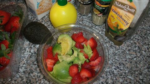 Eine Schüssel mit Erdbeer-Guacamole steht vor verschiedenen Zutaten wie Avocado, Zitronensaft und Gewürzen auf einer Arbeitsplatte.