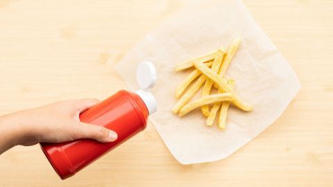 Ein roter Ketchupspender wird über einen Teller mit Pommes frites gehalten, um diese zu verfeinern.