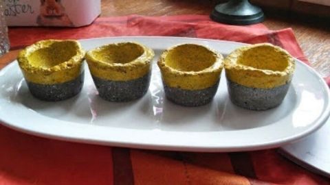 Vier Eierbecher aus Zement stehen auf einem weißen Teller. Sie sind grau mit goldenen Rändern und liegen auf einem bunten Tisch.