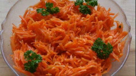 Frischer, geriebener Karottensalat ist in einer Glasschüssel angerichtet, garniert mit Petersilie und wirkt appetitlich.