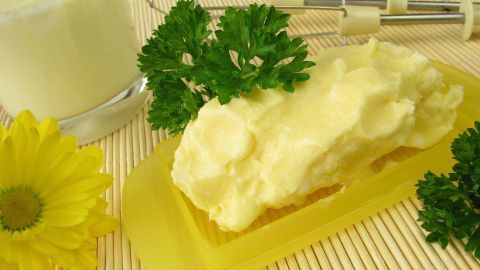 Butter liegt auf einem gelben Teller, während frische Petersilie und Sonnenblumen im Hintergrund dekorativ präsentiert werden.