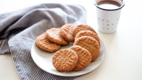 Auf einem weißen Teller liegen mehrere Erdnussbutter-Kekse. Neben dem Teller steht eine Tasse mit Getränk.