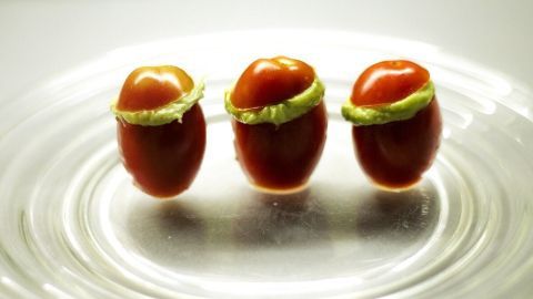 Mini-Tomaten stehen auf einem gläsernen Teller und sind mit cremigem Guacahummus gefüllt, serviert in ansprechender Anordnung.