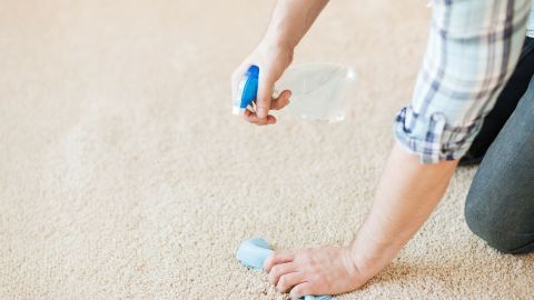 Eine Person sprüht Reinigungslösung auf einen Teppich, um Rußflecken zu entfernen und für Sauberkeit zu sorgen.