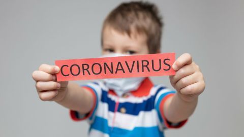 Ein Junge mit Mundschutz hält ein rotes Schild mit der Aufschrift „CORONAVIRUS“ in Richtung Kamera.