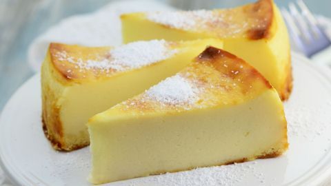 Käsekuchen ohne Boden liegt appetitlich auf einem Teller, bestreut mit Puderzucker und umgeben von leichter Dekoration.
