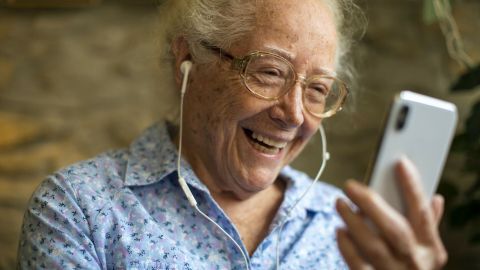 Eine ältere Frau lächelt und spricht über Videotelefonie mit ihren Enkeln, während sie ein Smartphone hält.