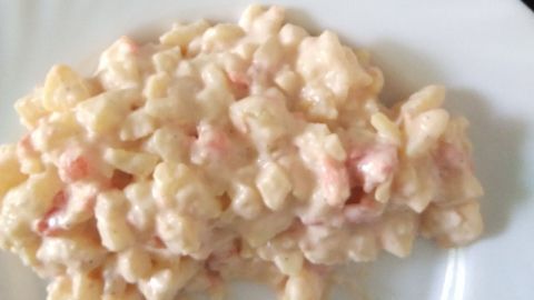 Ein cremiger Kartoffelsalat mit kleinen Stücken, der auf einem weißen Teller angerichtet ist, wirkt einladend und frisch.