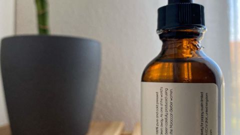 Braune Glasflasche mit Pipette steht auf einem Holzregal neben einem Pflanzentopf, unterstützt die Hautpflege gegen unreine Haut.