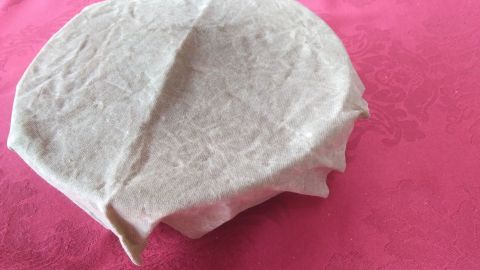 Ein Bienenwachstuch deckt eine runde Schüssel ab und schützt so Lebensmittel auf einer pinken Unterlage.