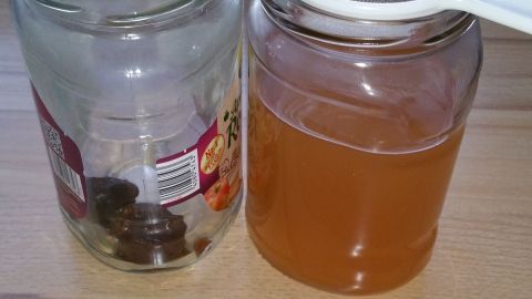 Ein Glas mit braunem Wildhefe-Ansatz steht neben einem leeren Glas auf einer Holzoberfläche, beide zur Hefeherstellung.