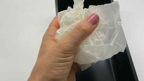 Eine Hand hält zerknülltes Backpapier über einer schwarzen Backform, bereit, es einzulegen, um Fett zu ersetzen.