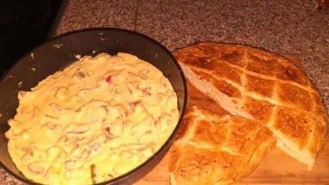 Eine Pfanne mit einer cremigen Paprika-Schmand-Mischung steht neben einem frisch gebackenem Brot auf einer Küchenoberfläche.