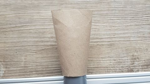 Eine selbstgemachte Aufsteckdüse wird auf ein graues Staubsaugerrohr gesteckt, auf einem holzfarbenen Tisch.