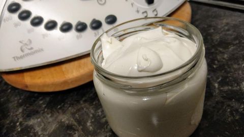 Ein Glas mit einer dicken, weißen Backtrennmittel-Creme steht auf einer dunklen Oberfläche neben einem Küchengerät.