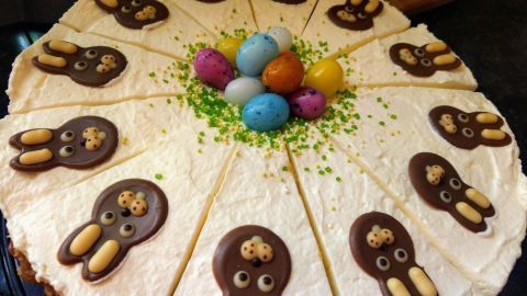 Ein Rhabarberkuchen mit bunten Schokoladenhasen und kandierten Eiern dekoriert, in einem frühlingshaften Ambiente platziert.
