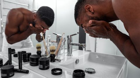 Ein junger Mann wäscht sich sein Gesicht im Badezimmer und nutzt Produkte für gesunde Haut, um seine Pflege zu optimieren.