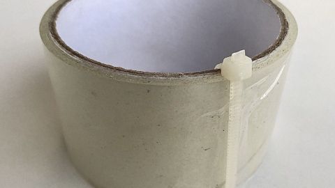Ein Klebeband-Rolle ist mit einem Kabelbinder gesichert, steht auf einem hellen Untergrund und zeigt eine praktische Lösung.
