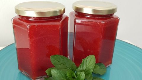 Zwei Gläser Erdbeer-Minz Marmelade stehen auf einem blauen Teller, umgeben von frischen Minzblättern.