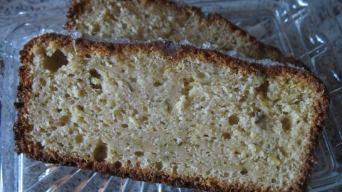 Zwei saftige Stücke Zucchini-Zitronen-Kuchen liegen auf einem transparenten Teller, umgeben von einer hellen, neutralen Umgebung.
