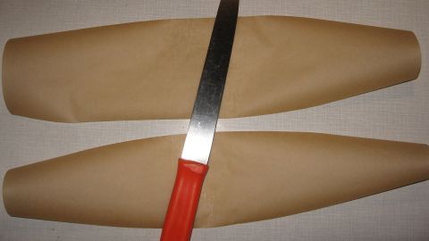 Zwei braune Papierstreifen liegen nebeneinander, während ein Küchenmesser mit rotem Griff auf einer der Kanten aufliegt.