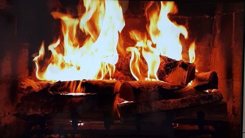 Ein TV-Bildschirm zeigt ein Kaminfeuer, das mit kräftigen Flammen Holzscheite verbrannt, gemütliche Atmosphäre verbreitet.