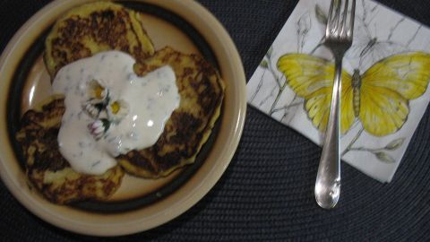 Kleine Kartoffel-Pfannenkuchen liegen auf einem Teller, garniert mit einer weißen Sauce, neben einer Serviette mit Schmetterling.