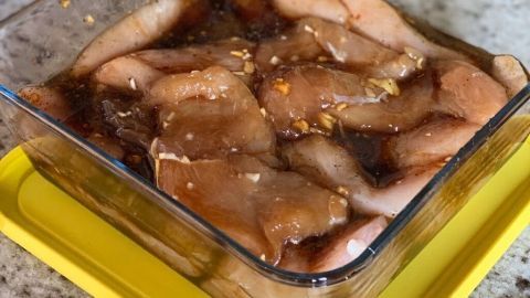 Marinierte Hähnchenstücke liegen in einer Schüssel mit Soja-Marinade auf einer Arbeitsplatte aus Stein.