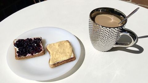 Ein Teller zeigt einen belegten Toast mit Eierlikör und Marmelade, daneben eine Tasse Kaffee auf einem Tisch im Freien.