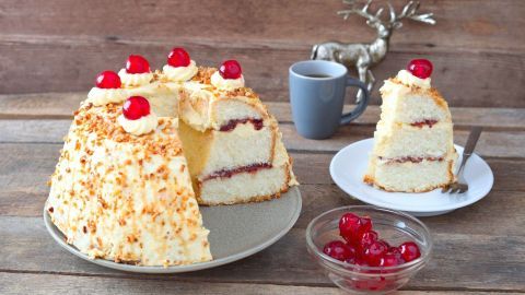 Ein Frankfurter Kranz steht auf einem Teller, während eine Portion neben einer Tasse Kaffee und einer Schüssel Kirschen präsent ist.
