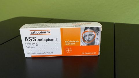 Ein Arzneimittelpackung mit ASS liegt auf einem Tisch vor einer grünen Wand, bereit zur Anwendung gegen Blutflecken.