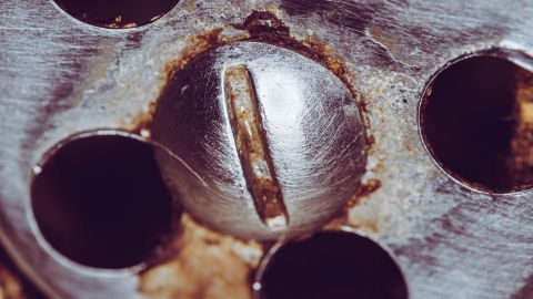 Eine verrostete Schraube sitzt fest in einer Metalloberfläche, während Eisspray auf die Schraube gesprüht wird, um sie zu lösen.