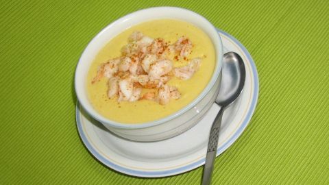 Eine Schüssel asiatische Maiscremesuppe mit gebratenen Garnelen steht auf einem weißen Unterteller und einem grünen Tisch.