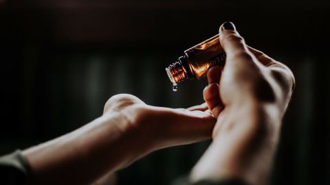 Eine Hand hält eine Flasche mit kosmetischem Öl und gibt einige Tropfen in die andere Hand, um die Haut zu pflegen.