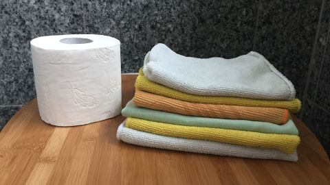 Ein Rollen Klopapier steht neben einem Stapel handtücher in einem modernen, hellen Küchenumfeld auf einem Holzbrett.